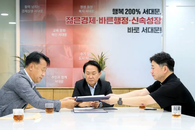 29일 서울 서대문구 구청장실에서 이성헌(가운데) 구청장의 중재로 홍제3구역 재건축 조합 대표자(왼쪽)와 무악재성당 대표자가 합의서를 교환하고 있다. 사진 제공=서대문구청