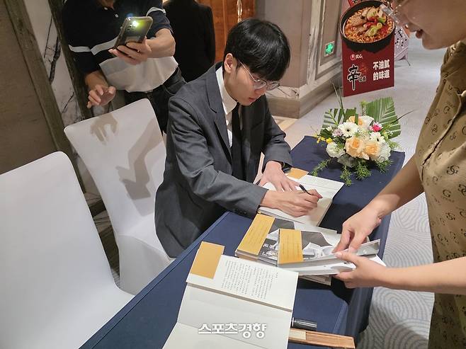신진서 9단이 2일 중국 칭다오의 쉐라톤 칭다오 자오저우 호텔에서 열린 대회 사전 기자회견이 끝난 후 자신의 자서전을 들고 찾아온 팬들에게 사인을 해주고 있다.     칭다오 | 윤은용 기자