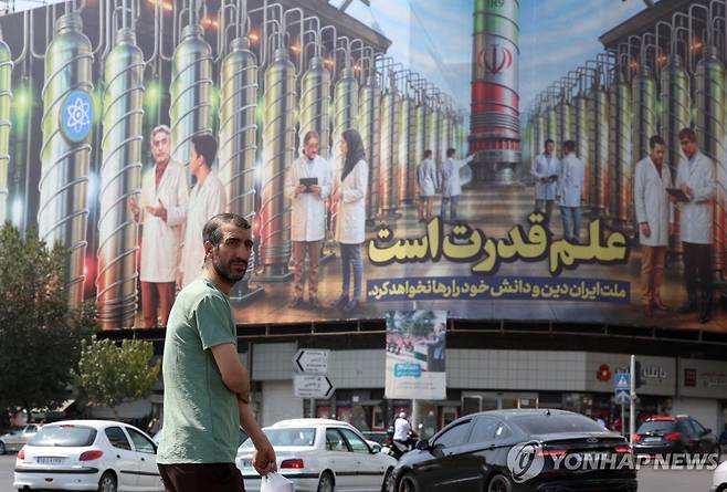 지난달 29일 이란 테헤란의 엥헬랍 광장에서 핵 원심분리기 사진과 함께 '과학이 힘이다'라고 적힌 광고판 앞을 한 행인이 지나가고 있다. [EPA=연합뉴스 자료사진]