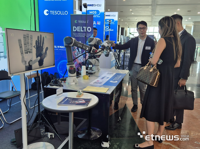'테솔로'의 자유자재로 움직이는 로봇 손에 관심을 기울이고 질문하고 있는 외국 참관객 모습.