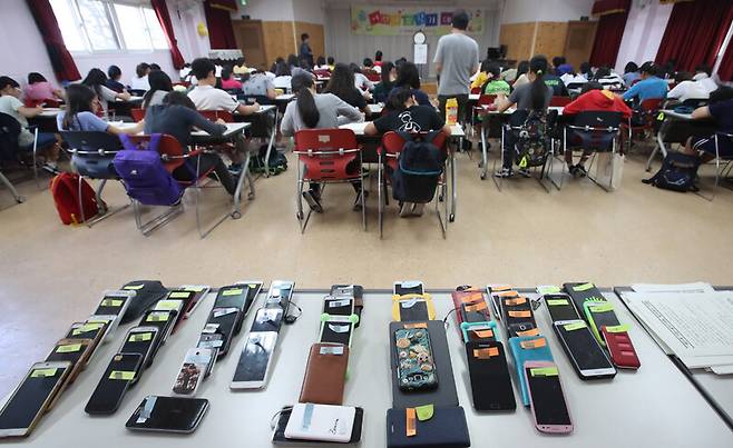 서울의 한 어린이도서관에 모인 초등학교 6학년 학생들 뒤로 수거된 스마트폰과 전자기기가 놓여 있다. 연합뉴스