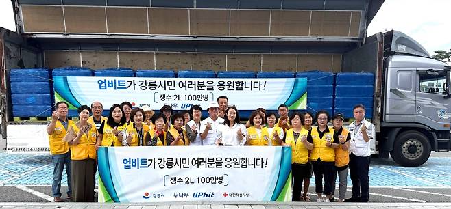 업비트가 강릉시에 생수 100만병을 기부, 대한적십자사 강릉지구봉사원 관계자들과 함께 기념 촬영을 하고 있다.