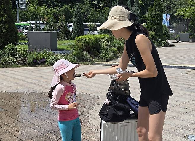 분수가 멈춘 사이 엄마가 아이의 입에 김밥을 넣어주고 있다.