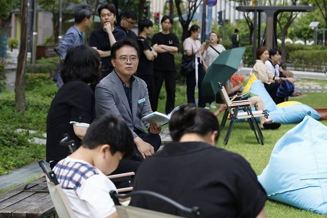 강서구 ‘하늘품은 야외도서관’ - 진교훈(가운데) 서울 강서구청장이 지난 6일 발산역 1번 출구 앞 마곡 문화의 거리에 조성된 ‘하늘품은 야외도서관’에서 책을 읽고 있다.  강서구 제공