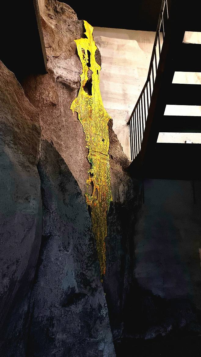 전기숙 작가의 현장 설치. 화산의 흔적 같은 바위벽 위로 노란 물질이 흐른다. 공간 자체가 생명의 흔적을 새로 기록하는 캔버스로 변한다. 장소가 곧 작품이 된다.