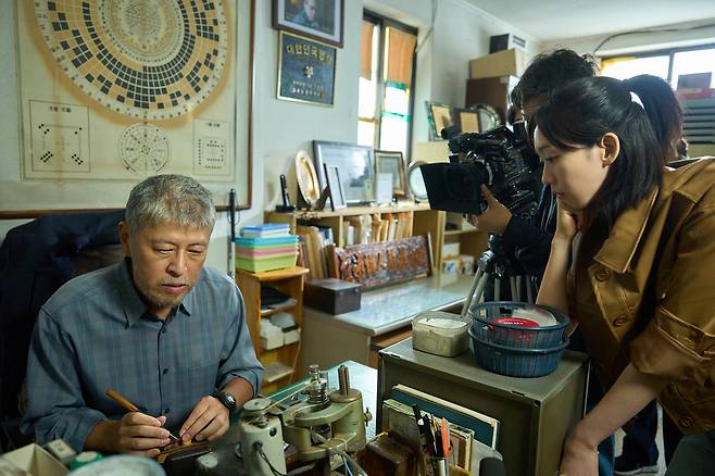 영화 <얼굴> 속 노인 임영규(권해효)가 김수진 PD(한지현)와의 인터뷰에서 도장 파는 시범을 포이고 있다. 플러스엠엔터테인먼트 제공