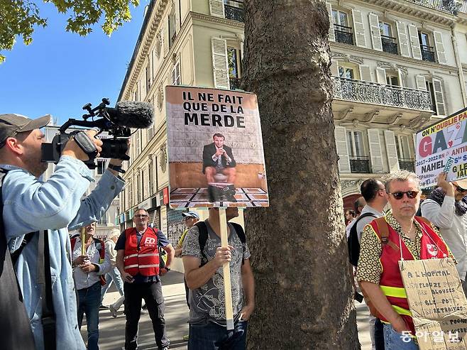 18일 프랑스 파리에서 열린 긴축 반대 시위에서 한 참가자들이 ‘그(에마뉘엘 마크롱 대통령)는 똥만 싼다’는 피켓을 들고 있다.  파리=유근형 특파원 noel@donga.com