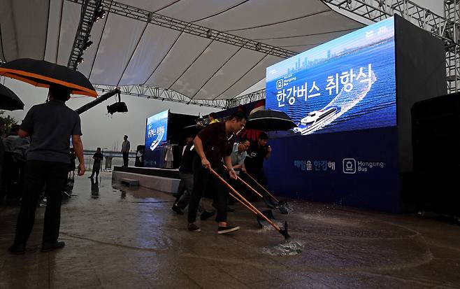 한강버스 취항식 행사장에서 관계자들이 넉가래로 연단 앞 빗물을 밀어내고 있다.