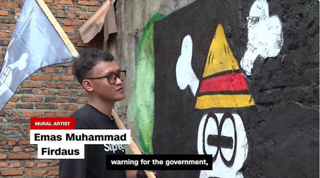 인도네시아 벽화가 에마스 무함마드 피르다우스가 ‘원피스’ 속 밀짚모자 해적단 깃발을 그린 졸리 로저 벽화를 완성하고 있다. 그는 ‘정부에 대한 경고의 상징’이라고 설명했다.  CNN 캡처