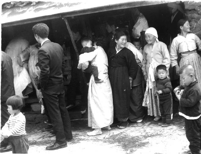 제주 가문잔치 모습 (제주=연합뉴스) 과거 제주에서 신부(맨 왼쪽 끝)가 신부상을 받기 위해 초가집의 풍체(차양) 아래를 지나 집 안으로 오를 때 신부를 보기 위해 아기를 안고 몸을 기울인 아주머니의 자세에서부터 어깨춤이라도 들썩일것 같은 표정과 몸짓의 할머니들의 모습, 마당에 모인 아이들의 모습이 담겨있다. [제주문화원, 제주민속자연사박물관 제공, 재판매 및 DB 금지]