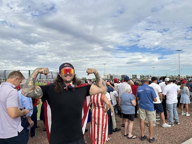 찰리 커크 추모식 입장을 대기 중인 카일 그리어씨 (글렌데일[미 애리조나주]=연합뉴스) 임미나 특파원 = 21일(현지시간) 오전 8시께 미국 애리조나주 피닉스 외곽 글렌데일의 스테이트팜 스타디움 앞에서 찰리 커크 추모식에 참석하려고 온 카일 그리어씨가 성조기를 어깨에 두른 채 웃어 보이고 있다. mina@yna.co.kr