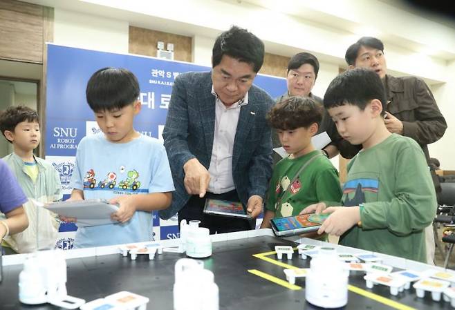 박준희 관악구청장(가운데)이 지난 19일 ‘2005 관악S밸리 창업페스티벌-로봇·AI 경진대회’에서 초등학생들에게 조종기 조작법에 대한 설명을 듣고 있다. 관악구 제공.