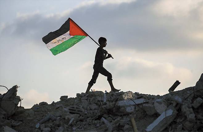 AFP 연합뉴스 22일 팔레스타인 가자지구 중부 부레이지 난민 캠프에서 팔레스타인 국기를 둘러멘 어린이가 파괴된 건물 잔해 위를 걷고 있다. 2023년 10월 시작된 이스라엘과 가자지구 무장 단체 하마스의 전쟁이 장기화하고 민간인 희생이 늘면서, 전날 영국·호주·캐나다·포르투갈에 이어 이날 프랑스도 팔레스타인을 국가로 공식 인정하고 이스라엘에 대한 외교적 압박에 나섰다.