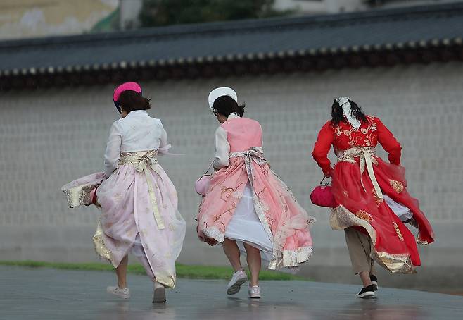 Foreign tourists in hanbok, Korean traditional attire, run to avoid the rain at Gwanghwamun Square in Jongno-gu, Seoul, on Sept. 16. (Yonhap)