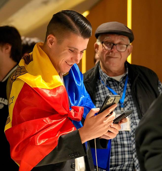 28일 동유럽 몰도바의 수도 키시너우에서 친유럽 성향의 집권당 ‘행동과 연대당(PAS)’ 지지자가 국기를 두른 채 휴대전화로 총선 개표 결과를 확인하며 미소짓고 있다. 이날 실시된 총선에서 PAS는 친러 성향 ‘애국블록’을 누르고 과반 의석을 확보할 것으로 보인다. 
키시너우=AP 뉴시스