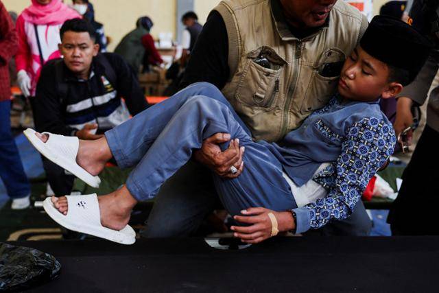 25일 인도네시아 서자바주 반둥의 임시 진료소에서 한 경찰이 정부 지원 무상급식을 먹고 식중독에 걸린 학생을 안아 옮기고 있다. 반둥=로이터 연합뉴스