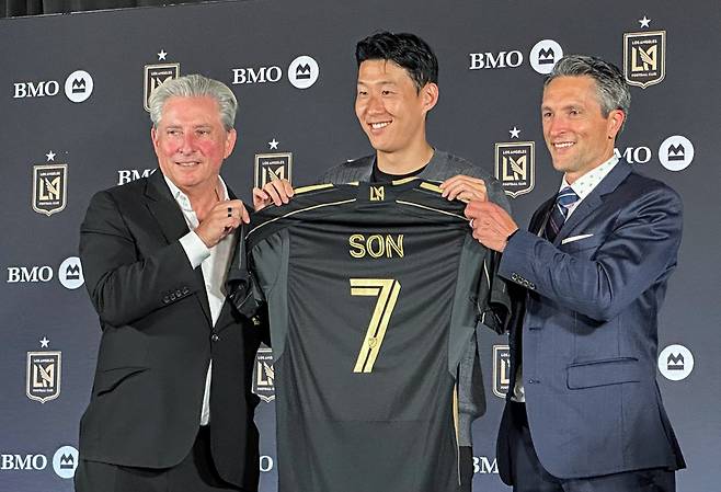 손흥민(가운데)이 지난달 6일 미국 로스앤젤레스(LA) BMO 스타디움에서 열린 LAFC 입단 기자회견에서 공동 구단주인 베넷 로즌솔과 존 소링턴 사이에서 등번호 7번이 새겨진 유니폼을 들고 있다. LA | 연합뉴스