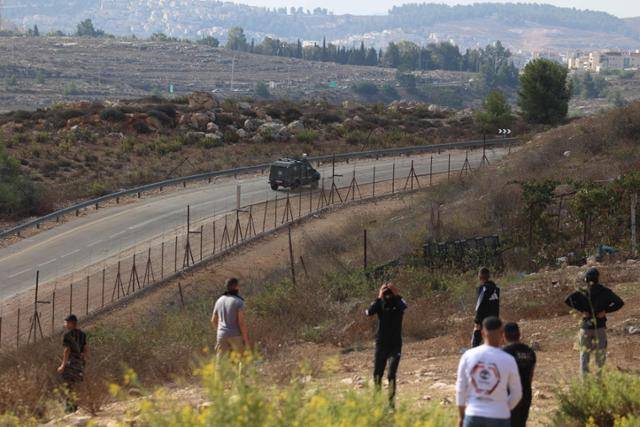 팔레스타인 청년들이 13일 이스라엘군 장갑차가 요르단강 서안지구에 위치한 오페르 군 교도소 밖 도로를 순찰하는 모습을 지켜보고 있다. 서안지구=AFP 연합뉴스