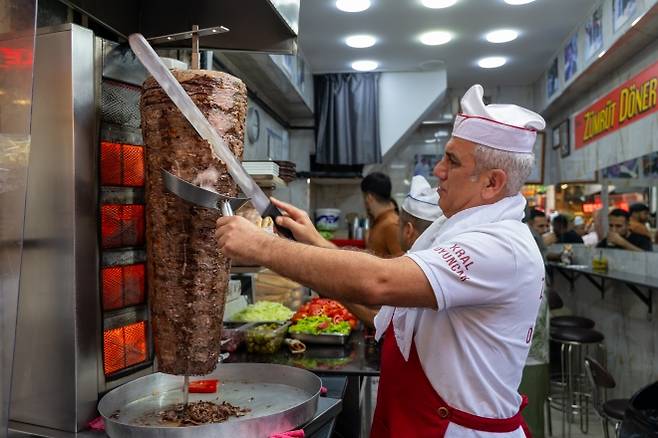 수직 회전 꼬치 도네르 케밥을 만들고 있는 요리사의 모습. 지방과 육즙이 아래에 있는 고기로 타고 흘러 수평으로 고기를 구울 때보다 촉촉함을 더 오래 유지할 수 있다. 여러 설이 있지만 19세기 오스만 제국 도시화 과정에서 수직 로티세리(회전 구이)가 조리 효율성을 이유로 자연스럽게 발전했다는 게 학계 입장이다.