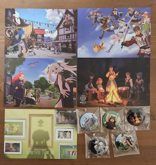 - 은색 봉투에 들어 있는 굿즈들. "엽서 5종, 캔뱃지 5종이 들어 있었다 마비노기 모바일 굿즈라는 게 없는 상황이기에 받은 것만으로도 기쁘다"