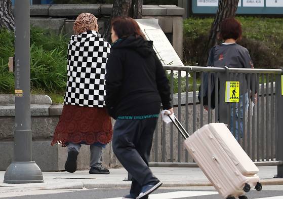 A pedestrian wraps a blanket around her shoulders while moving near City Hall Station in Seoul amid the morning chill on Oct. 20. [NEWS1]