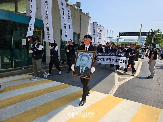 김영훈 한전KPS비정규직지회장이 지난 6월 18일 고 김충현씨 영정 사진을 들고 사고 현장 방문을 마친 뒤 태안화력발전소 정문을 나서고 있다. ⓒ뉴시스
