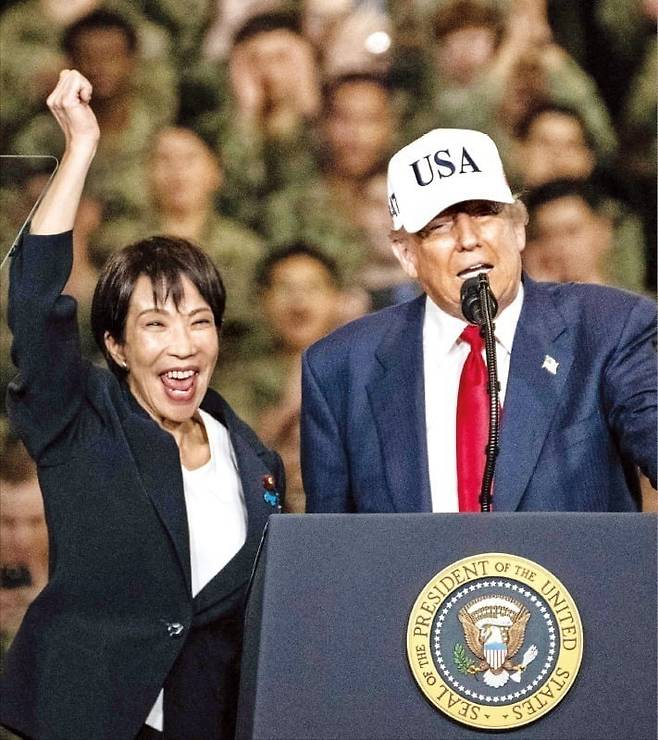 < 더 밀착한 美·日 > 다카이치 사나에 일본 총리가 28일 도널드 트럼프 미국 대통령이 요코스카 미 해군기지에 정박한 핵추진 항공모함 ‘USS조지워싱턴호’에서 연설하는 도중 손을 들어 환호하고 있다. 두 정상은 앞서 정상회담을 한 뒤 미 대통령 전용 헬기 ‘마린원’을 타고 요코스카 해군기지로 함께 이동했다.  AFP연합뉴스