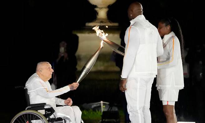 2024년 7월 27일 파리 올림픽 개막식 당시 1948년 런던 올림픽 금메달리스트 샤를 코스테(왼쪽)가 프랑스&nbsp;스포츠 영웅이자 성화 최종 점화자인 마리 호세 페렉(오른쪽)과 테디 리네르(가운데)에게 성화봉을 건네고 있다. AP연합뉴스