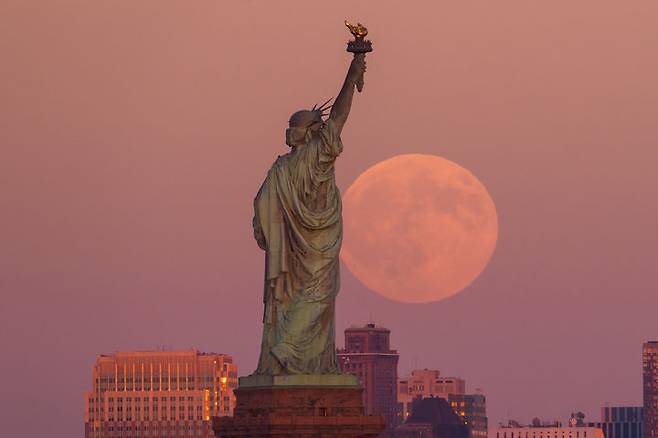 [저지시티=AP/뉴시스] 6일(현지 시간) 미 뉴저지주 저지시티에서 자유의 여신상과 브루클린 스카이라인 뒤로 슈퍼문이 떠오르고 있다. 2025.10.07.