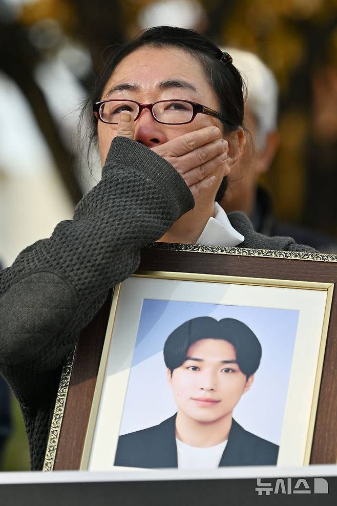 [광주=뉴시스] 이영주 기자 = 6일 오전 광주 북구 전남대학교 후문에서 열린 민주사회를위한변호사모임 광주지부의 전남대 교수 갑질 사건 진상규명 촉구 기자회견, 교수의 갑질로 숨진 대학원생 고(故) 이대원씨의 어머니가 이씨의 영정사진을 안은 채 눈물을 닦고 있다. 2025.11.06. leeyj2578@newsis.com