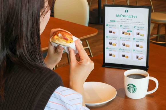 스타벅스 모델이 모닝 세트로 구입한 '베이컨 체다 & 오믈렛 샌드위치'와 '카페 아메리카노'를 즐기고 있다. [사진=스타벅스]