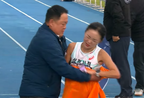 23일 인천 송도에서 열린 '2025 인천국제마라톤' 여자 국내부 경기에서 1위로 골인한 삼척시청의 이수민(오른쪽) 선수가 결승선을 통과한 직후의 모습. 김완기 감독이 이 선수에게 타월을 두르며 잡아주자 이 선수가 얼굴을 찌푸리며 뿌리치고 있다. KBS스포츠 유튜브 캡처