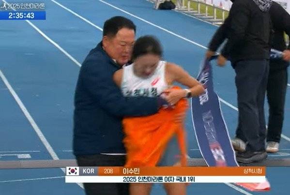 Kim Wan-ki (left), head coach of Samcheok City Hall’s track team, wraps a towel around runner Lee Su-min after she finishes first in the Korean women’s elite full-course race at the 2025 Incheon International Marathon at the Incheon Munhak Sports Complex on Sunday. (KBS)