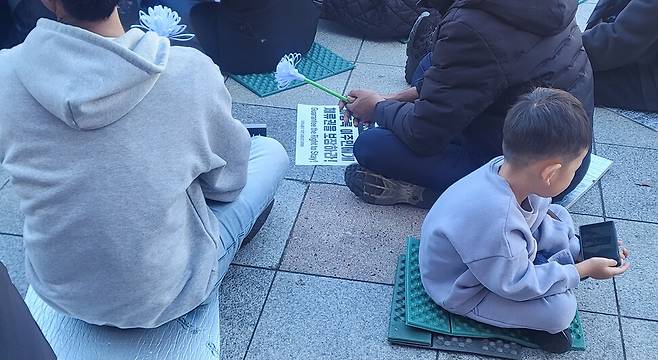 지난 16일 대구시 달서구 성서공단역 앞에서 열린 고 뚜안씨의 거리 추모제에서 부모와 함께 온 아이가 휴대폰을 보고 있다. 이문영 기자