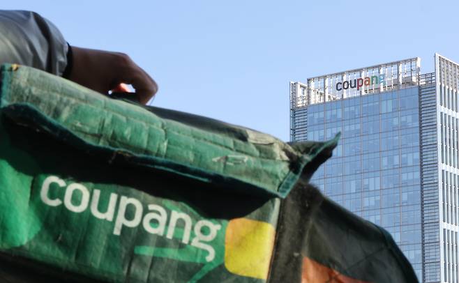 A reporter holds up a Coupang Rocket Fresh Bag in front of the company's headquarters in Songpa District, southern Seoul, on Dec. 1. [YONHAP]