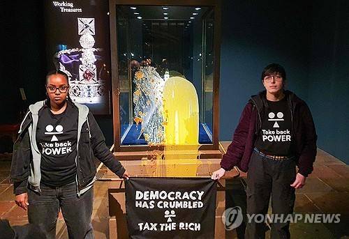 시위대에 봉변 당한 英왕실 왕관 진열장 영국 시민단체 '테이크 백 파워' 활동가들이 런던탑에서 값비싼 영국 왕실 왕관 진열장에 음식물을 뿌린 뒤 '민주주의가 바스러졌다. 부자들에게 과세하라'라는 구호가 적힌 펼침막을 들고 있다. ['테이크 백 파워' 제공/AFP=연합뉴스. 재판매 및 DB 금지]