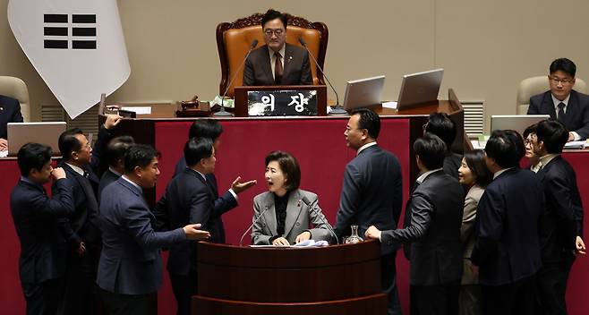 Lawmakers from rival parties crowd around the podium and raise their voices as Rep. Na Kyung-won of the People Power Party, center front, stages a filibuster against proposed amendments to the Fair Transactions in Franchise Business Act during a plenary session at the National Assembly on Dec. 9. [YONHAP]