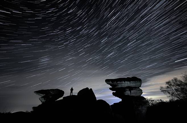 한 남성이 영국 노스요크셔 니더데일 자연경관보호구역에 있는 브림햄 록스 위로 쌍둥이자리 유성우가 쏟아지는 동안 유성을 바라보고 있습니다. /로이터=뉴스1
