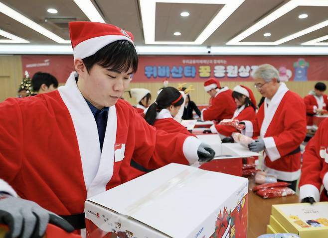 자립준비청년 조규환씨가 지난 8일 우리금융미래재단의 ‘우리금융 위비산타 출정식’에 참여해 임종룡 우리금융그룹 회장(오른쪽) 등과 전국 아동양육시설에 전달할 선물 상자를 포장하고 있다.  우리금융 제공
