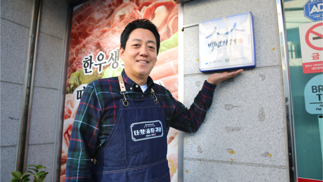 ‘따귀탕’으로 유명한 ‘타향골’ 조병근 대표가 가게 앞 백년가게 현판을 소개하고 있다.