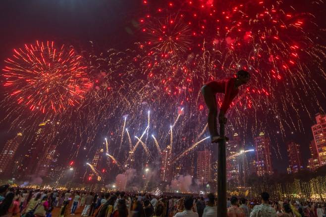 지난 10월 20일(현지 시간) 인도 뭄바이에서 디왈리 빛축제가 열려 불꽃놀이가 하늘을 수놓은 가운데 한 소녀가 기둥에 올라가 인도 전통 체조 '물라캄' 동작을 수행하고 있다. /AP=뉴시스