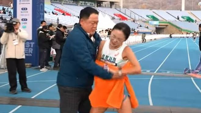 지난 11월 23일 열린 2025 인천국제마라톤대회에서 결승선을 통과한 이수민 선수가 부축하기 위해 감싸안는 김완기 감독의 손을 뿌리치고 있다. /KBS스포츠 유튜브