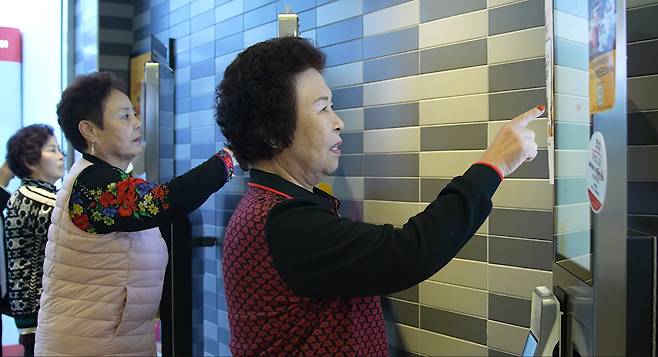 Elderly participants practice placing orders using a self-service kiosk during a training session at a fast-food restaurant in the greater Seoul area. [NATIONAL INSTITUTE FOR LIFELONG EDUCATION]