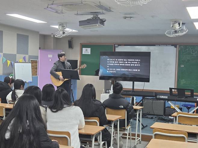 최새롬 학원복음화인큐베이팅 대표가 인천의 한 중학교 음악실에서 통기타를 메고 학생들과 함께 찬양을 부르고 있다.