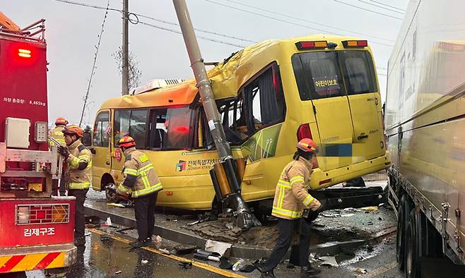 23일 오후 4시26분쯤 전북 김제시 백산면 상정리 지평선산단로 돌제교차로에서 초등학교 스쿨버스가 화물 윙바디 트럭과 충돌한 뒤 안전지대에 세워진 신호등과 추돌하는 사고가 나자 119 구급대원들이 분주하게 움직이고 있다. 전북도소방본부 제공