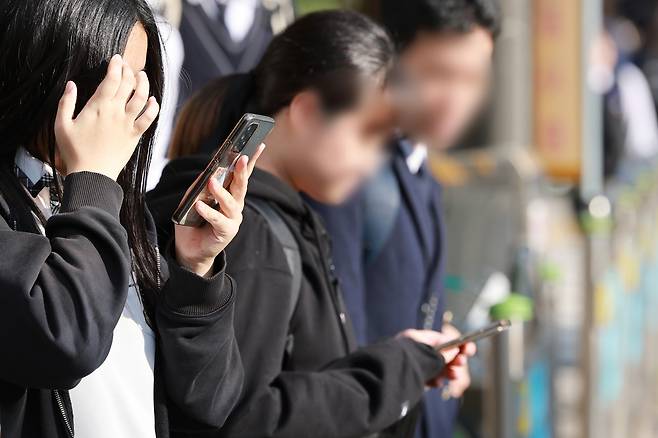 Students are seen on their phones on a street in front of a middle school in Seoul on Nov. 4, 2024. [YONHAP]