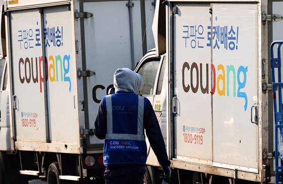 A Coupang Logistics Center worker is seen next to Coupang delivery trucks in Seoul on Dec. 17. [YONHAP]