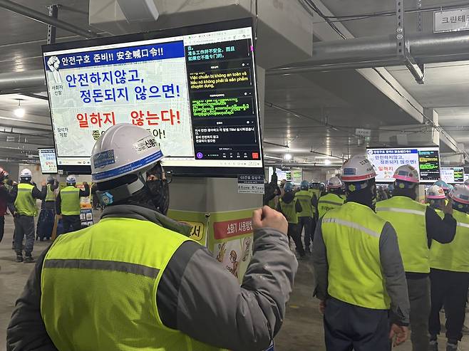 지난달 19일 서울 마포구 공덕동 ‘마포자이힐스테이트라첼스’(공덕1구역) 공사현장에서 진행된 TBM 모습. 곳곳에 설치된 모니터 오른편에는 작업반장의 공지사항이 중국어, 베트남어, 미얀마어로 동시통역되고 있다. 신혜원 기자