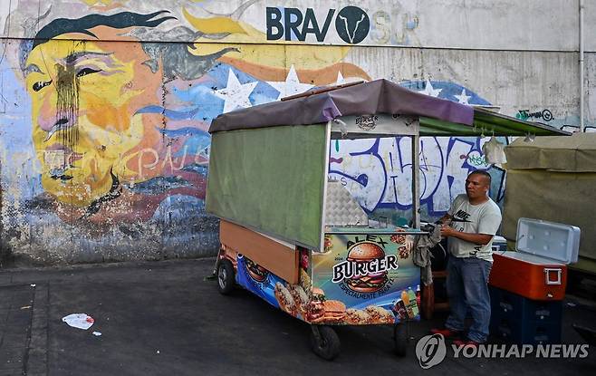 지난해 12월 29일(현지시간) 차베스 벽화 앞에서 햄버거 파는 상인 [카라카스 AFP=연합뉴스. 재판매 및 DB 금지]