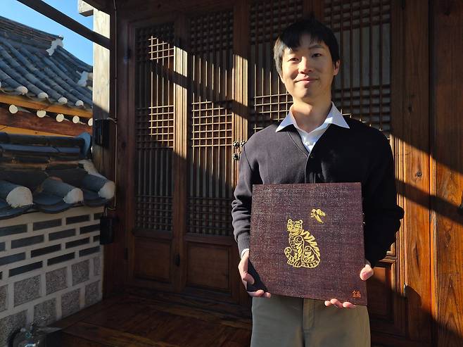 금박장 전수장학생 김진호(27)씨가 지난달 26일 서울 종로구 북촌한옥마을의 '금박연'에서 금박 작품 '까치와 호랑이'를 들고 서 있다. 김씨는 최근 국가무형유산기능협회가 미국 워싱턴 주미대한제국공사관에서 주최한 광복 80돌 기획전 ‘한국적 환대의 아름다움’에 이 작품을 출품했다. 세계적 인기를 누린 애니메이션 ‘케이팝 데몬 헌터스’의 호랑이 캐릭터 ‘더피’의 원형이어서 많은 관심을 받았다. /김관래 기자